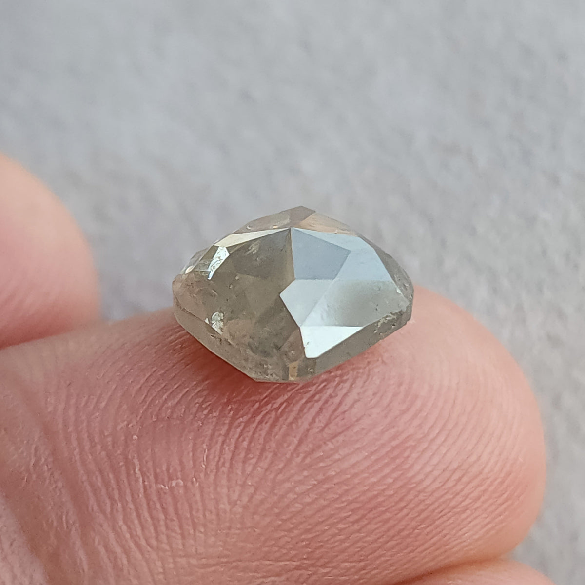 Oblique view of the cushion diamond on a fingertip, showing the raised opposing facets and part of its depth.