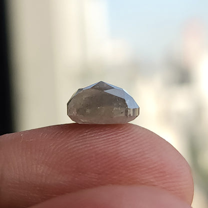 Low side profile of the cushion diamond resting on a fingertip, showing its raised faceting and overall depth.