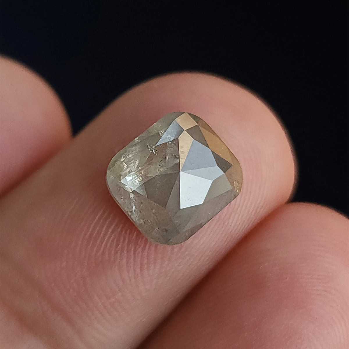 Opposing faceted side of the cushion diamond on a fingertip against a dark background, with bright triangular reflections.