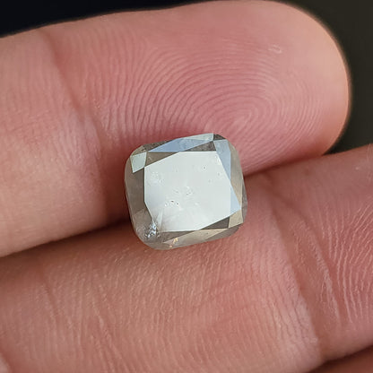 Wider front view of the cushion diamond held against fingers, showing its scale and a broad white table reflection.