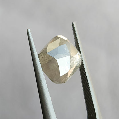 Opposing faceted side of the cushion diamond held in tweezers, with triangular pale reflections across its raised surface.