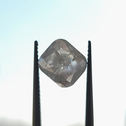 Cushion diamond viewed from its opposing faceted side in upright tweezers against a bright background, showing inclusion detail.