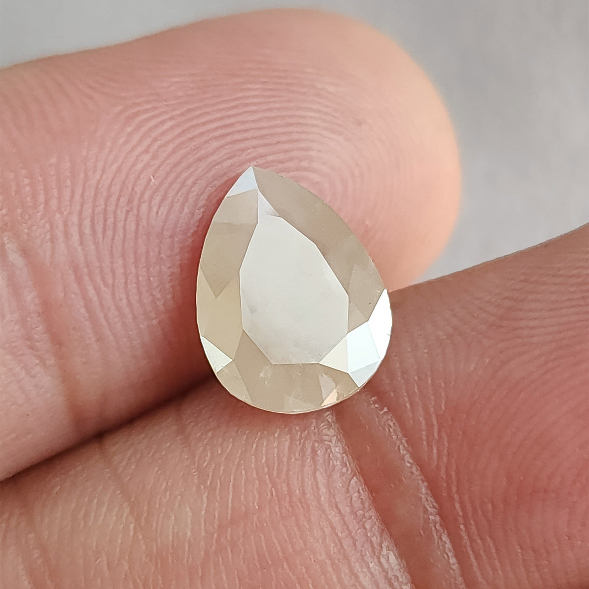Pear-shaped ice gray diamond held by fingers, showing a broad pale flat table and bright surrounding facets.