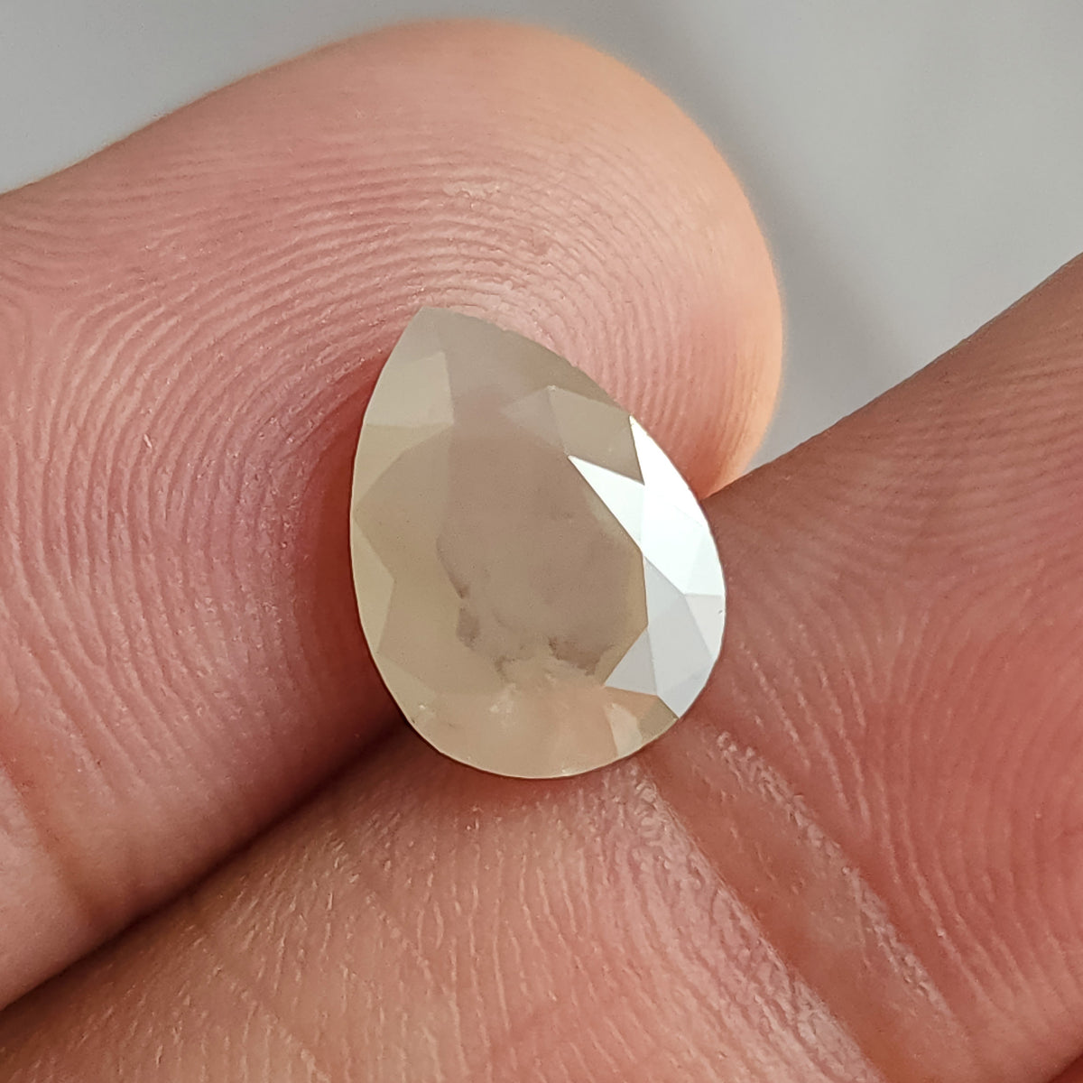 Face-up pear-shaped ice gray diamond held by fingers, with dark inclusions visible through the broad flat table.