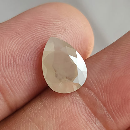 Face-up pear-shaped ice gray diamond held by fingers, with dark inclusions visible through the broad flat table.
