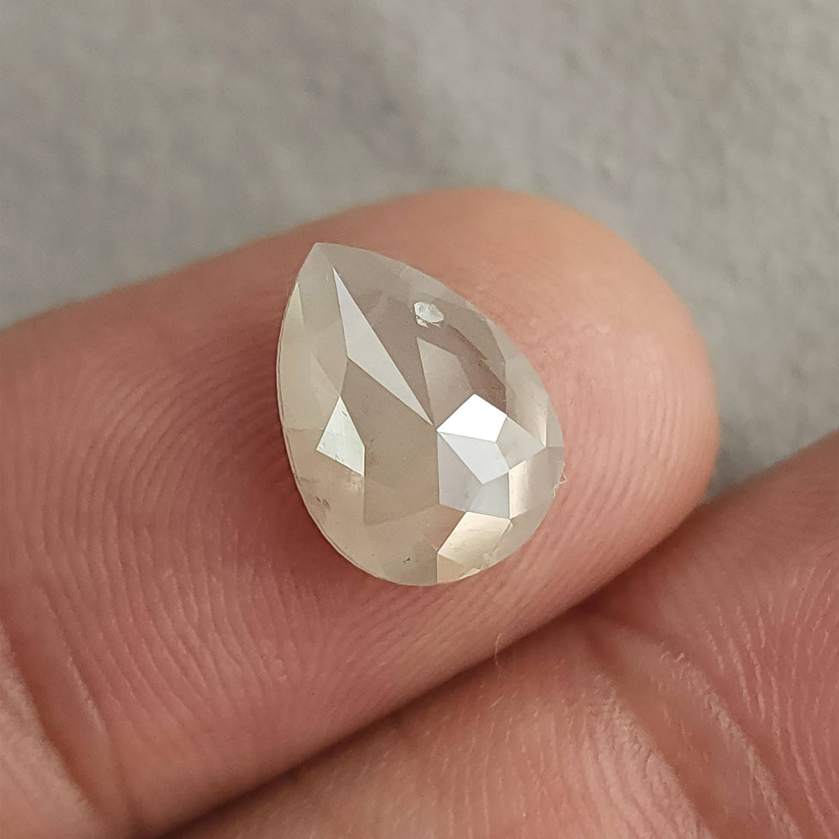 Rose-cut pavilion of a pear-shaped ice gray diamond on a fingertip, showing triangular facets meeting toward the center.