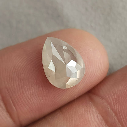 Rose-cut pavilion of a pear-shaped ice gray diamond on a fingertip, showing triangular facets meeting toward the center.