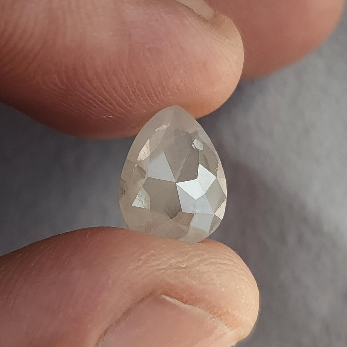 Pear-shaped ice gray diamond held between fingers with its rose-cut pavilion facing the camera.
