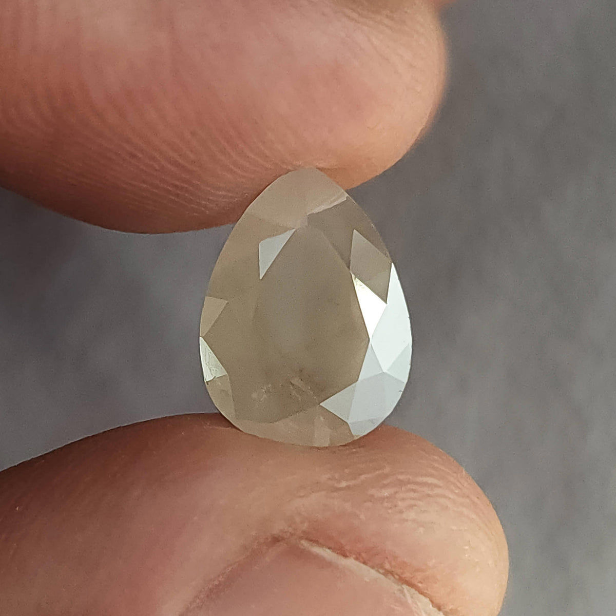Table-side view of a pear-shaped ice gray diamond between fingers, with a muted central table and bright right border.