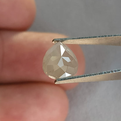 Rose-cut pavilion of a pear-shaped ice gray diamond in tweezers against fingers, showing converging triangular facets.