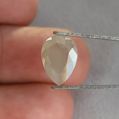 Table-side pear-shaped ice gray diamond in tweezers, with the point downward and a bright right-edge reflection.