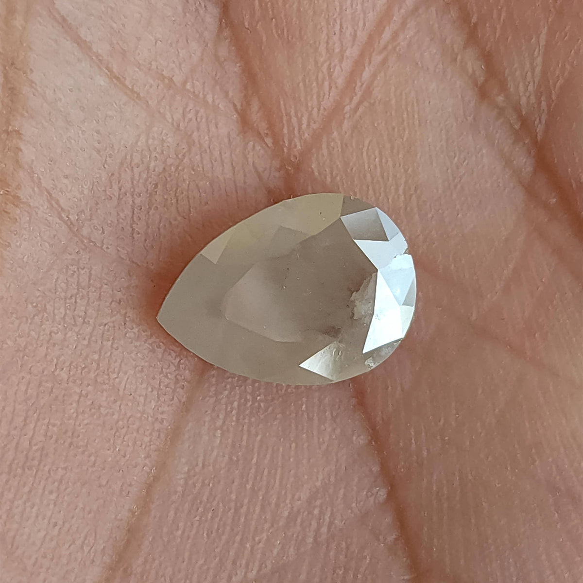 Table-side pear-shaped ice gray diamond lying sideways on a hand for scale, showing its broad flat central table.