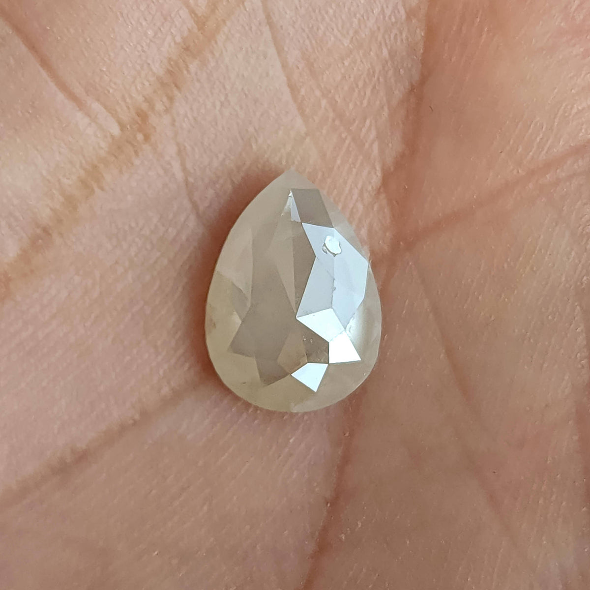 Rose-cut pavilion of a pear-shaped ice gray diamond resting upright on a hand, with a bright central facet.
