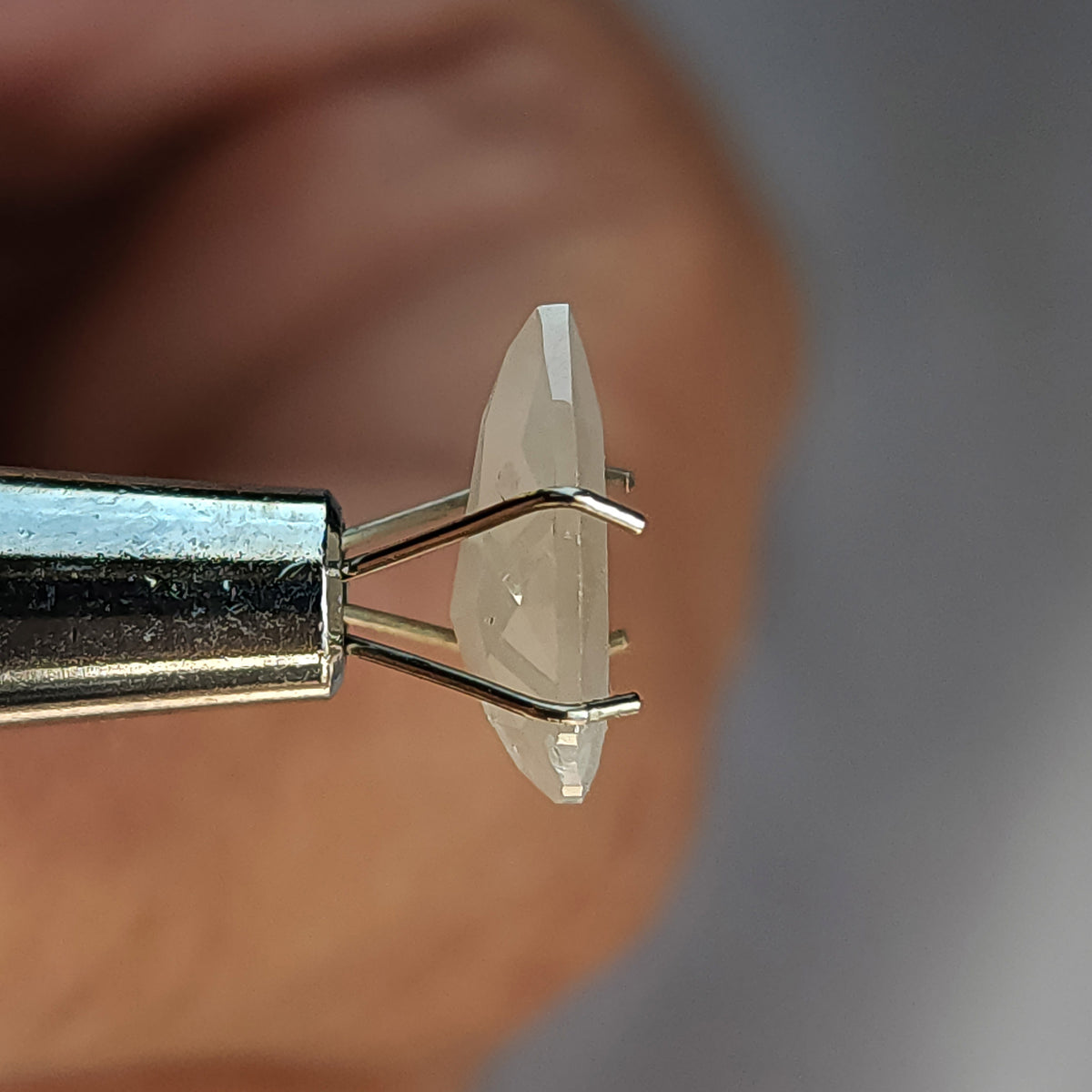 Edge-on profile of a pear-shaped ice gray diamond in a temporary prong holder, showing its two differently faceted sides.