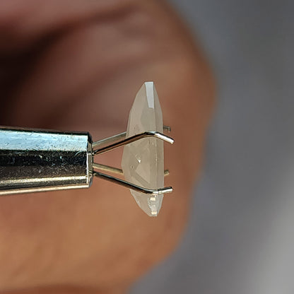Edge-on profile of a pear-shaped ice gray diamond in a temporary prong holder, showing its two differently faceted sides.