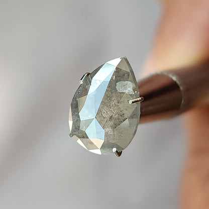 Oblique view of the pear diamond in a temporary stone holder, showing large reflective facets on the rose-cut opposing side.