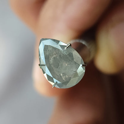 Pear diamond in a temporary holder at a changed front angle, with dark inclusions visible through its table side.