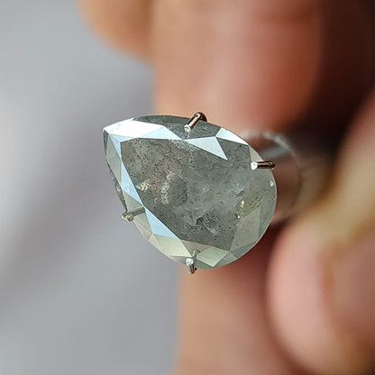 Tilted front view of the pear diamond in a temporary holder, showing the table side, gray inclusions and bright outer facets.