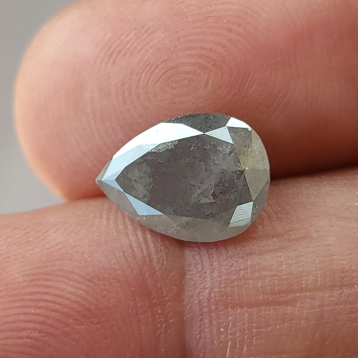 Pear-shaped diamond resting table-side up against fingertips for scale, with visible inclusions and bright edge facets.