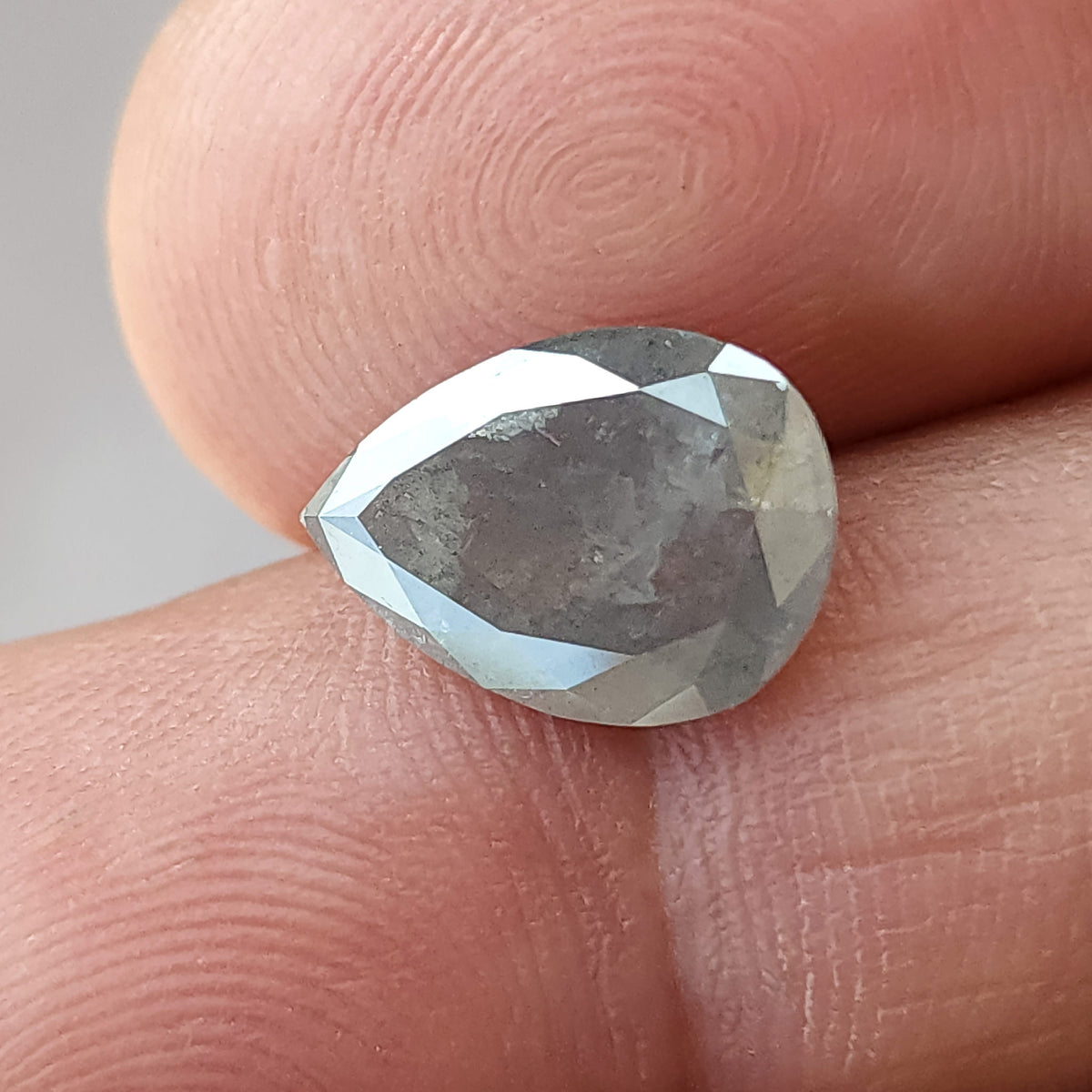 Alternate front view of the pear diamond on fingertips, showing its scale, gray center and pale reflections around the edges.