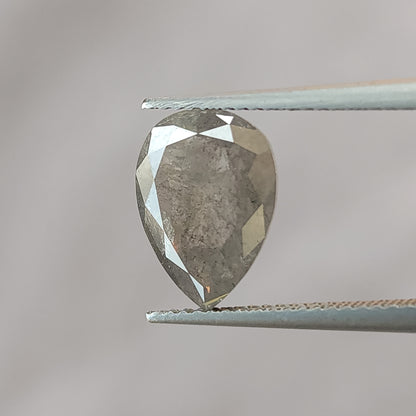 Pear-shaped salt and pepper diamond held face-up in tweezers against gray, with its brilliant-cut table side and inclusions visible.