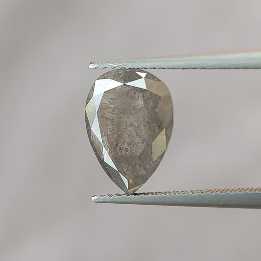 Pear-shaped salt and pepper diamond held face-up in tweezers against gray, with its brilliant-cut table side and inclusions visible.