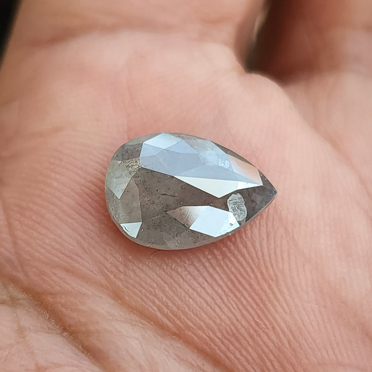Pear diamond resting on a palm with its rose-faceted pavilion side uppermost, showing large bright facets across the raised surface.