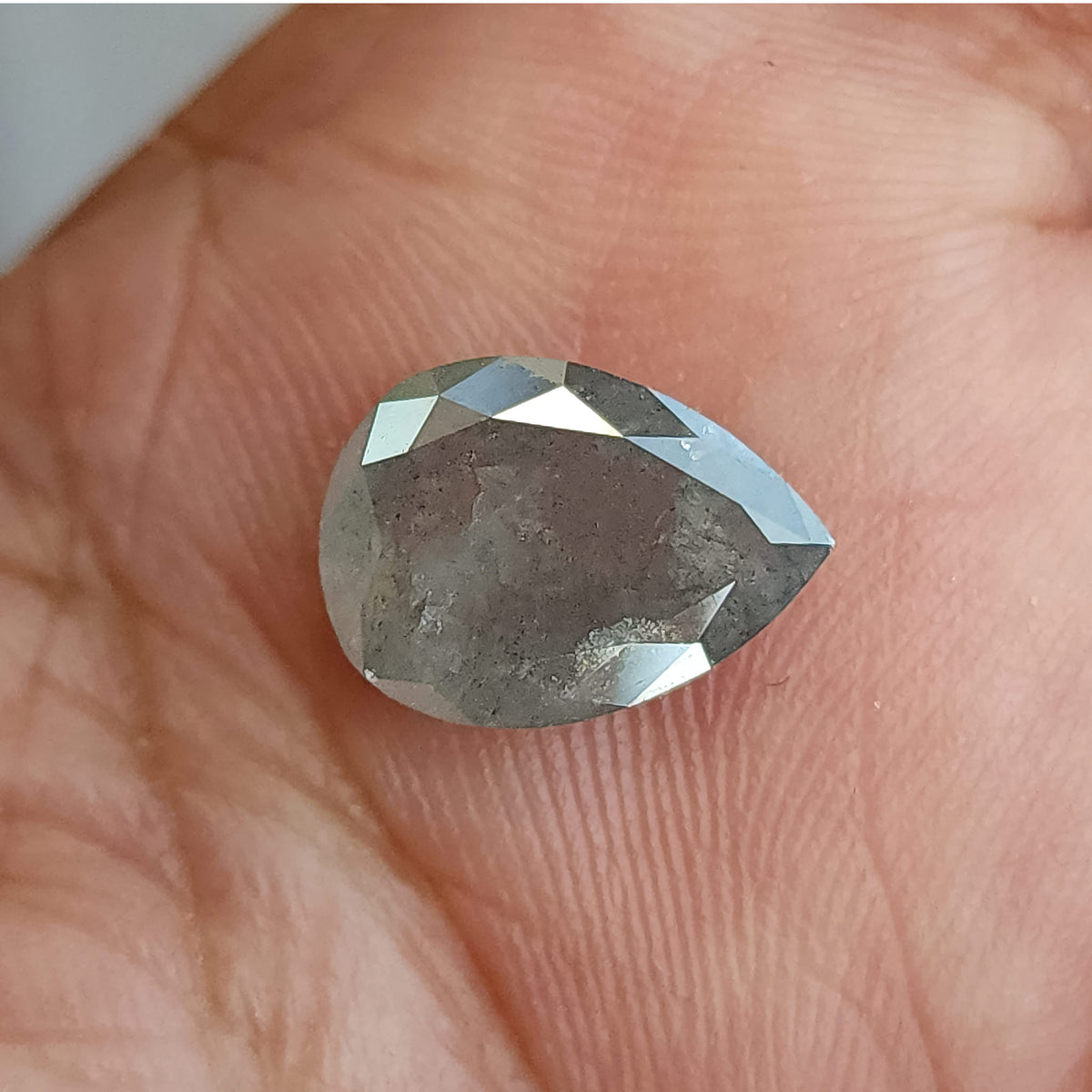 Pear-shaped diamond resting table-side up on a palm, with gray inclusions visible beneath bright border reflections.