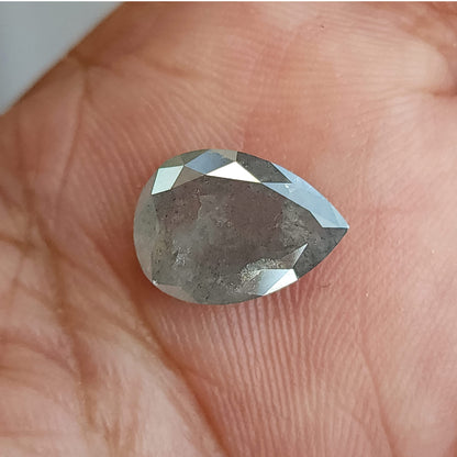 Pear-shaped diamond resting table-side up on a palm, with gray inclusions visible beneath bright border reflections.