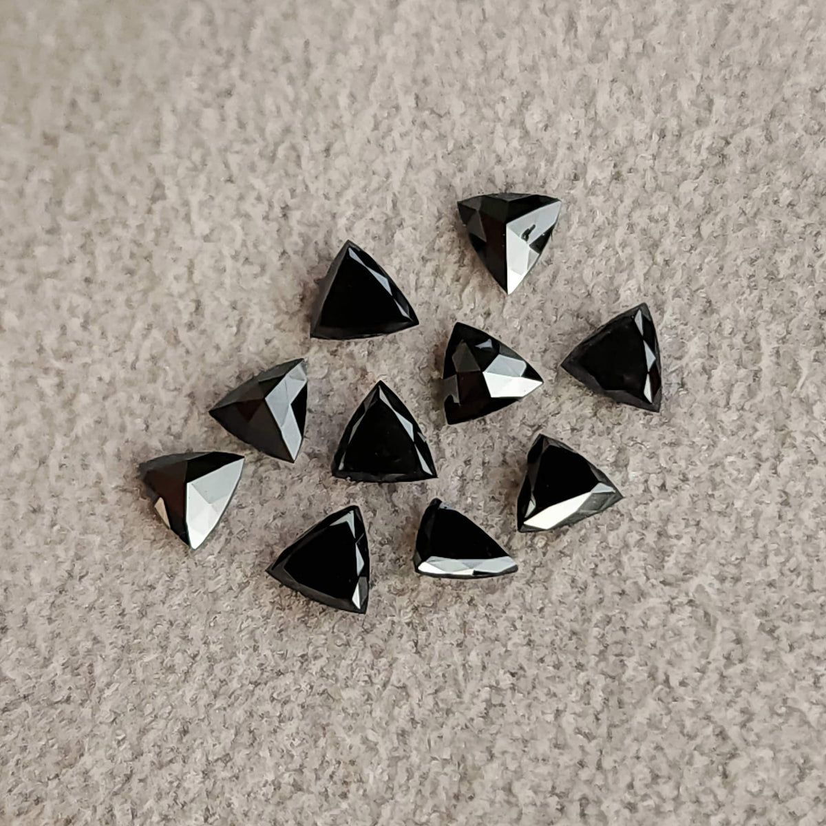 Black trillion diamonds scattered on textured pale fabric, with mixed dark faces and silver reflections.
