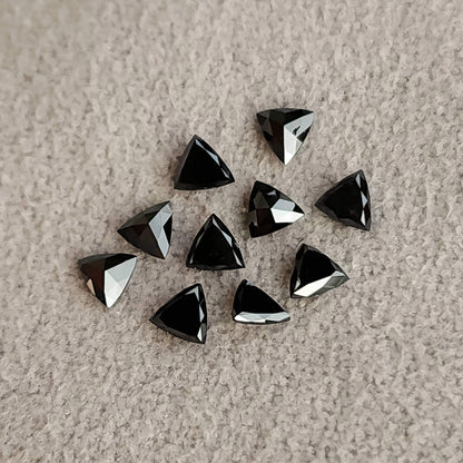 Black trillion diamonds scattered on textured pale fabric, with mixed dark faces and silver reflections.