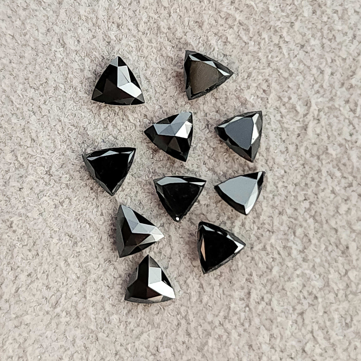 Loose black trillion diamonds on fabric, viewed at varying angles with angular bright reflections.