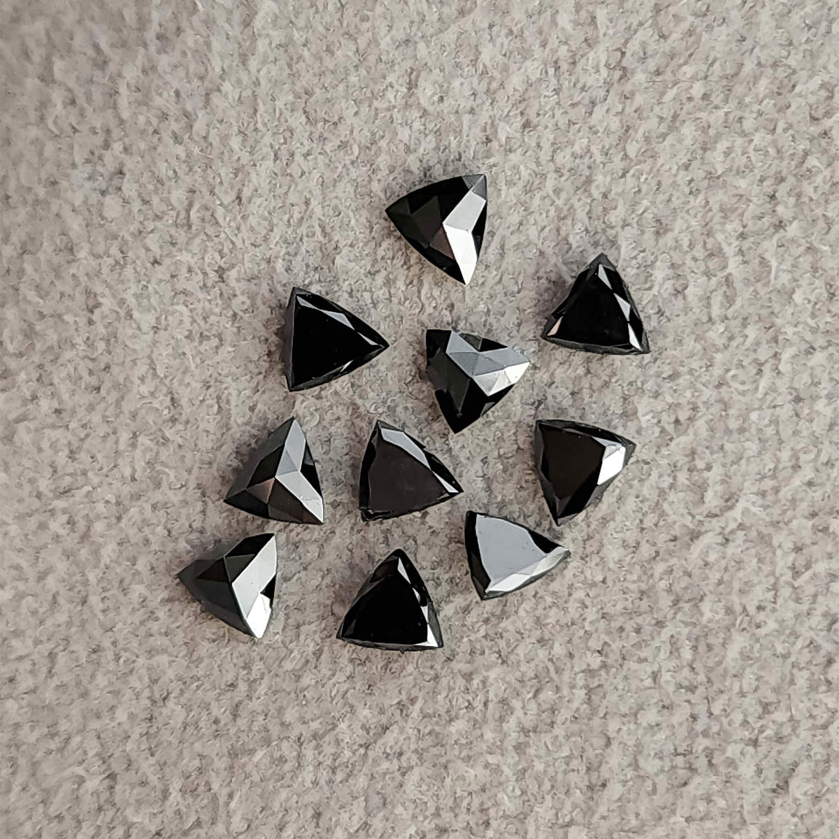 Group of black trillion diamonds on textured fabric, showing both dark flat faces and more strongly reflected facets.