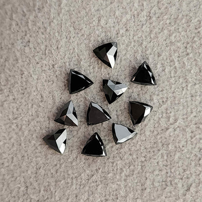 Group of black trillion diamonds on textured fabric, showing both dark flat faces and more strongly reflected facets.