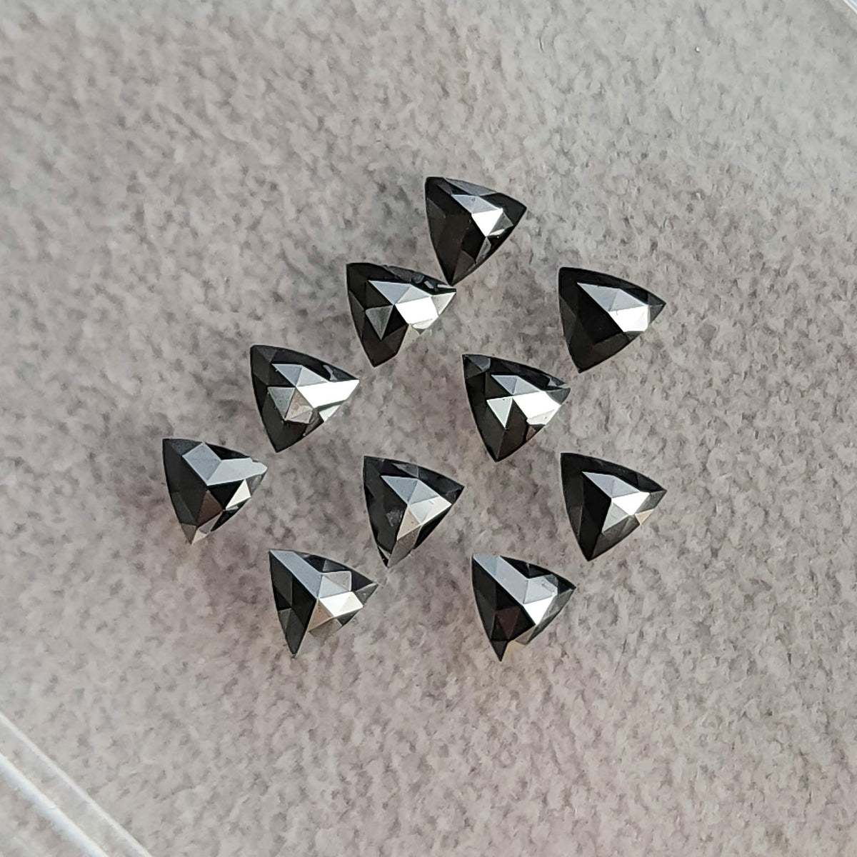 Black trillion diamonds on fabric with the converging triangular facets of their rose-cut pavilion sides visible.