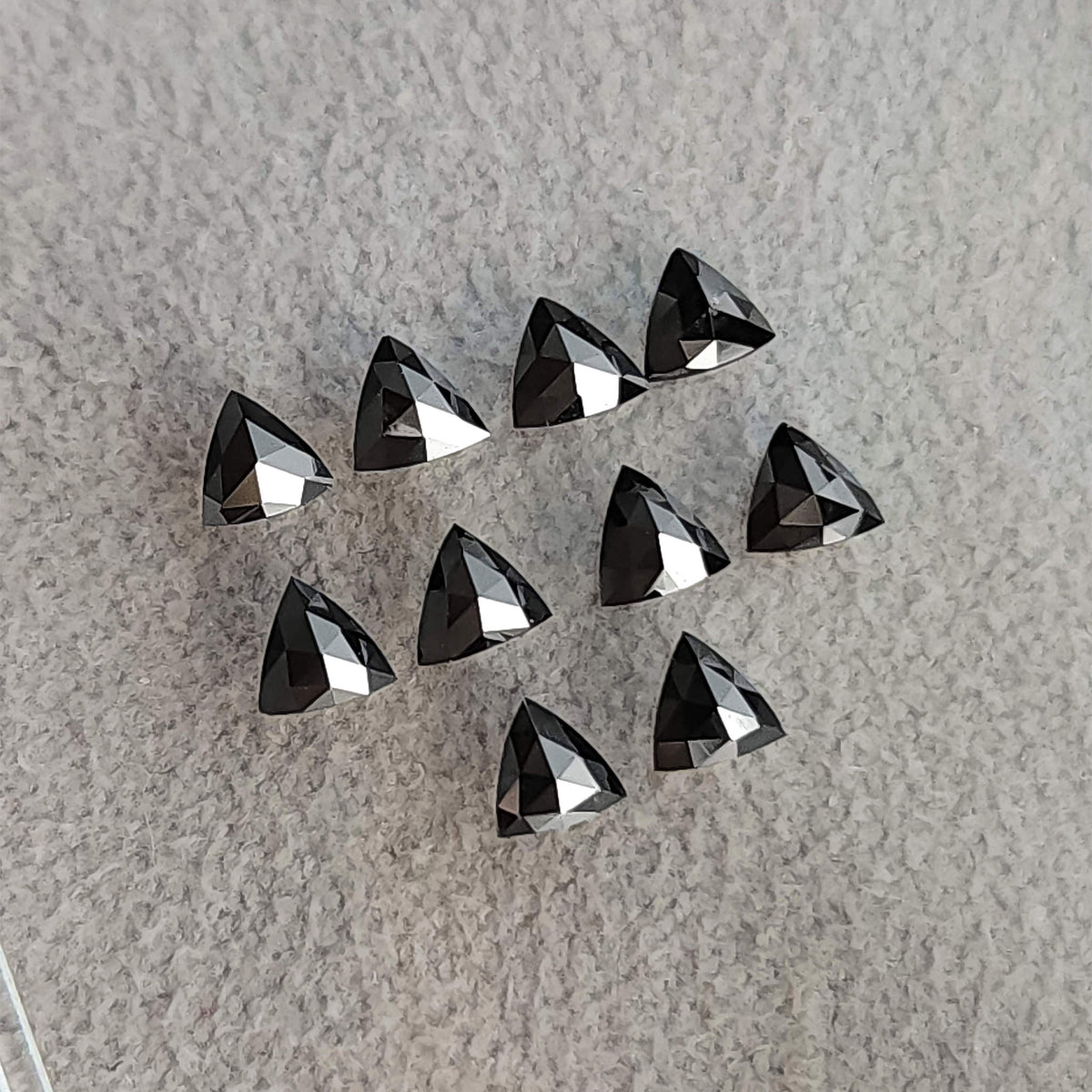 Two loose rows of black trillion diamonds showing rose-cut pavilion facets against pale textured fabric.