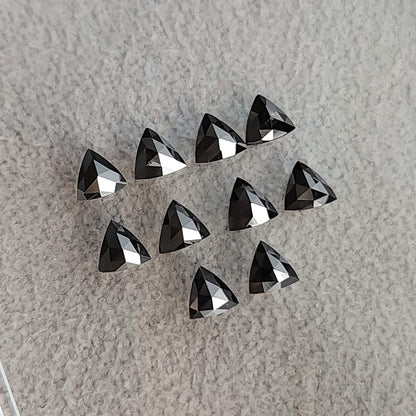 Two loose rows of black trillion diamonds showing rose-cut pavilion facets against pale textured fabric.