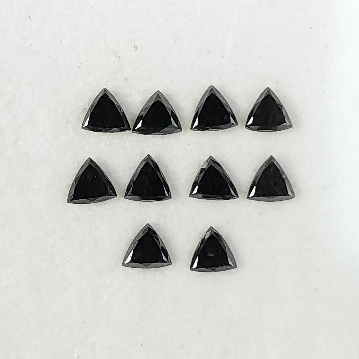 Ten black trillion diamonds arranged on a white surface, showing their flat triangular tables and surrounding crown facets.