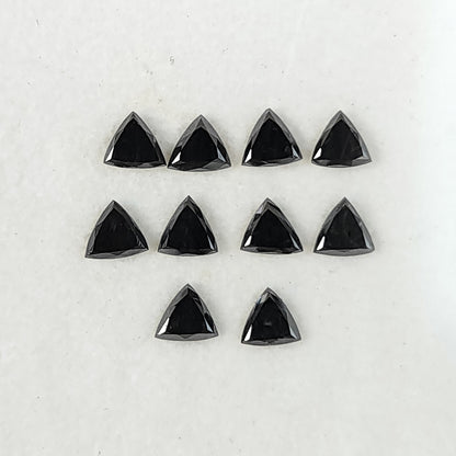 Ten black trillion diamonds arranged on a white surface, showing their flat triangular tables and surrounding crown facets.