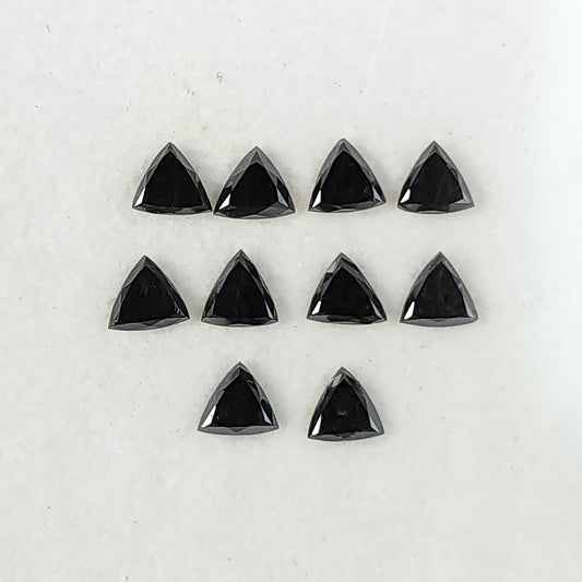 Ten black trillion diamonds arranged on a white surface, showing their flat triangular tables and surrounding crown facets.