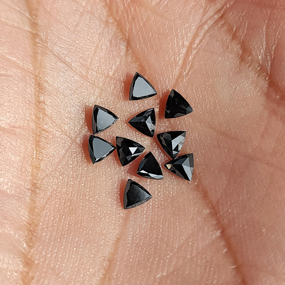 Black trillion diamonds grouped on a palm for relative scale, showing a mixture of flat tables and pointed faceted backs.