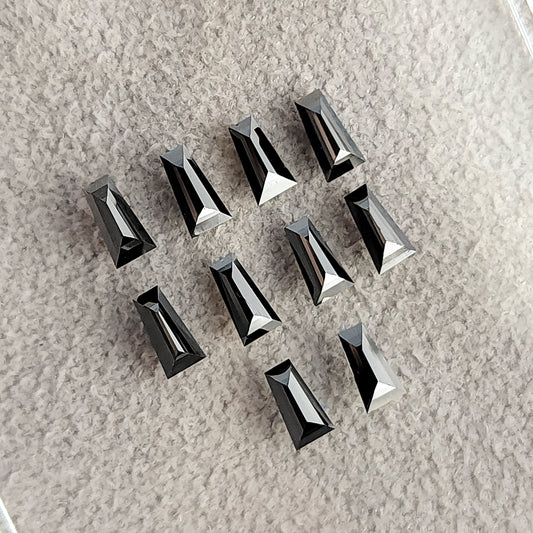 Black tapered baguette diamonds arranged on a pale textured surface, with bright narrow facet reflections.