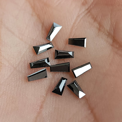 Black tapered diamonds resting in a palm, showing size and changing facet reflections.