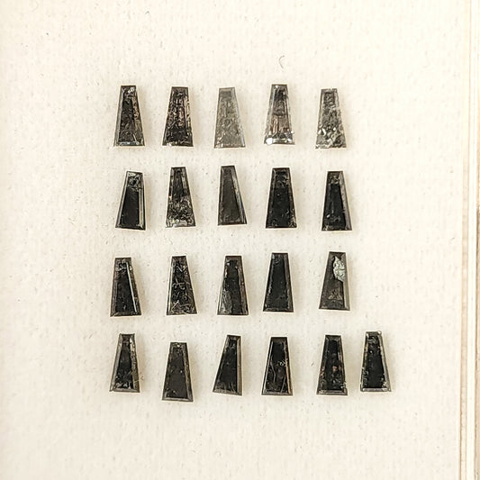 Group of natural salt and pepper tapered baguette diamonds arranged in a display box, showing mixed smoky gray tones.
