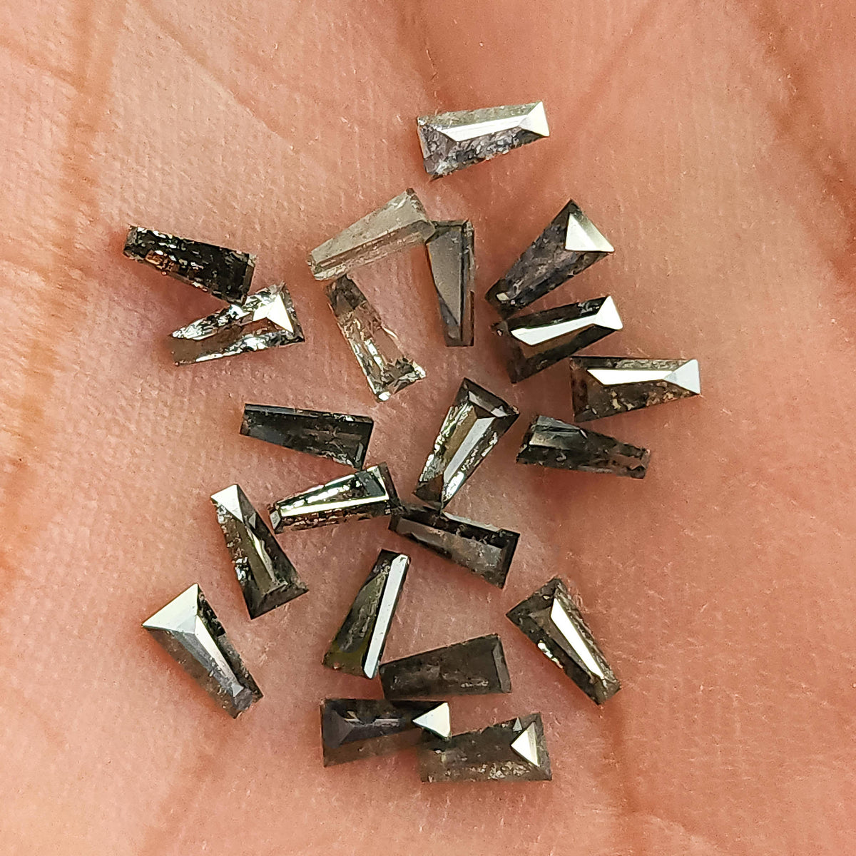 Close view of several tapered baguette diamonds with varied gray and black inclusion patterns and reflective facets.
