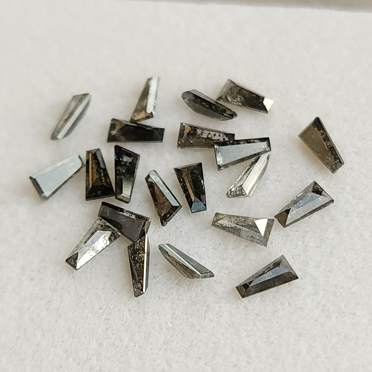 Small group of natural tapered baguette diamonds showing variation in smoky gray tone and salt and pepper inclusions.