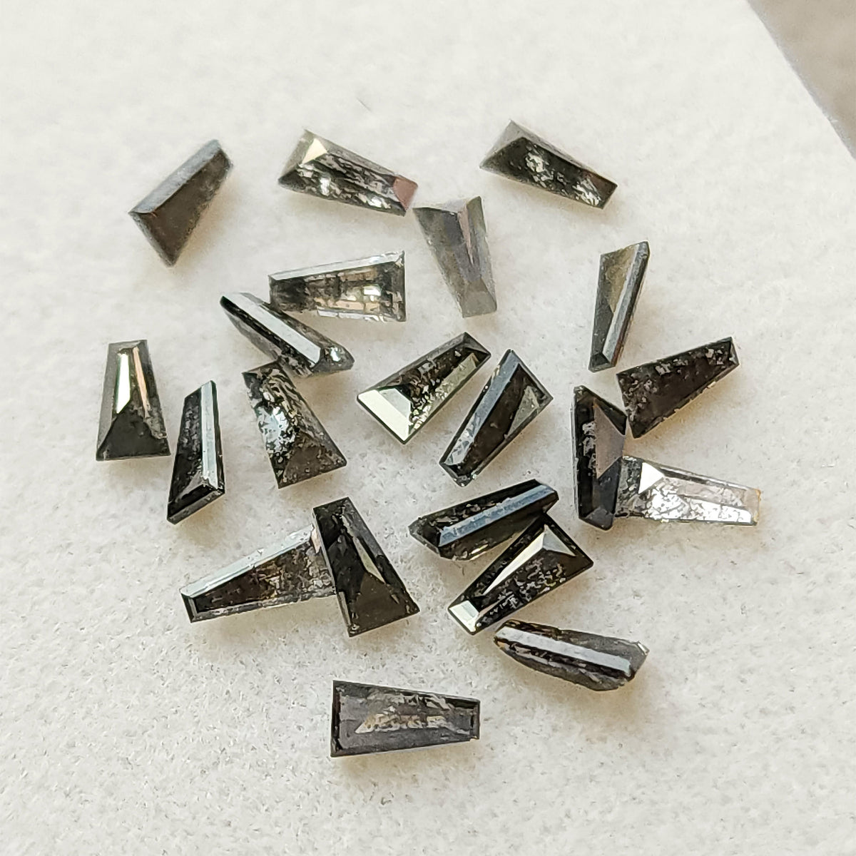 Loose arrangement of faceted tapered baguette diamonds with varied dark inclusion patterns.