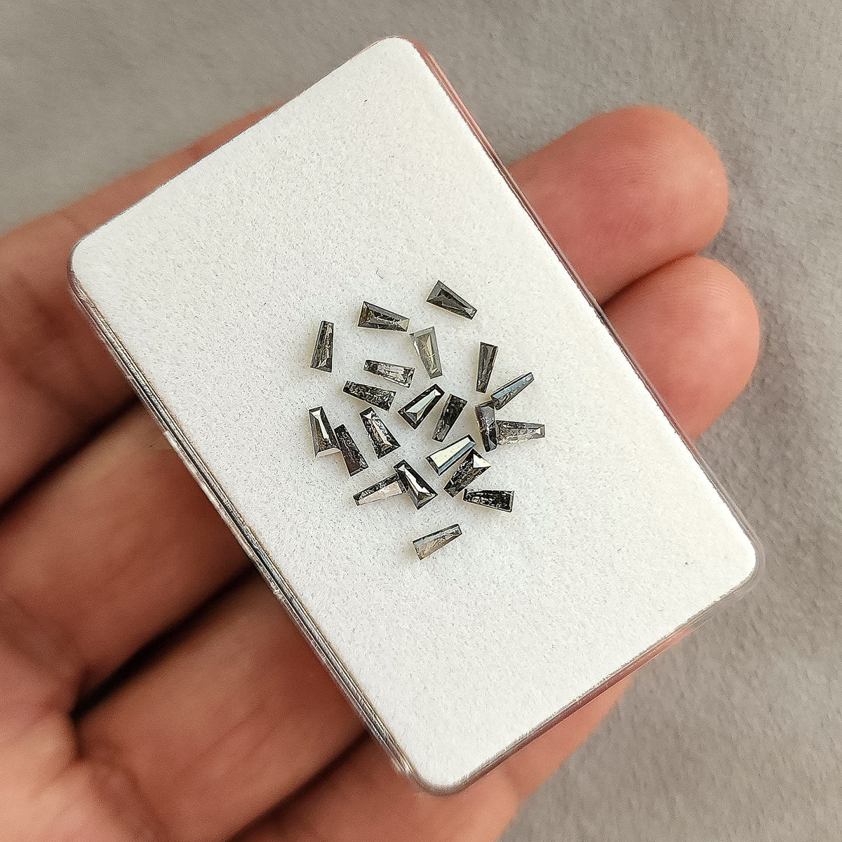 Natural salt and pepper tapered baguette diamonds beside a hand and display box for size context.