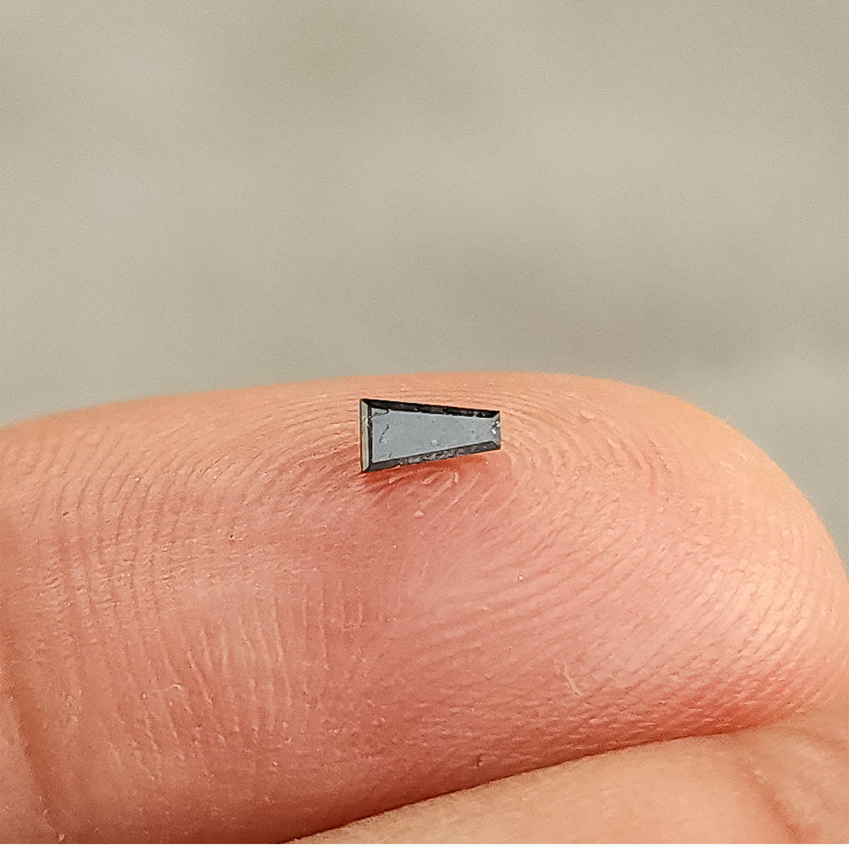 Single natural salt and pepper tapered baguette diamond held against a hand, showing its faceted outline and dark inclusions.