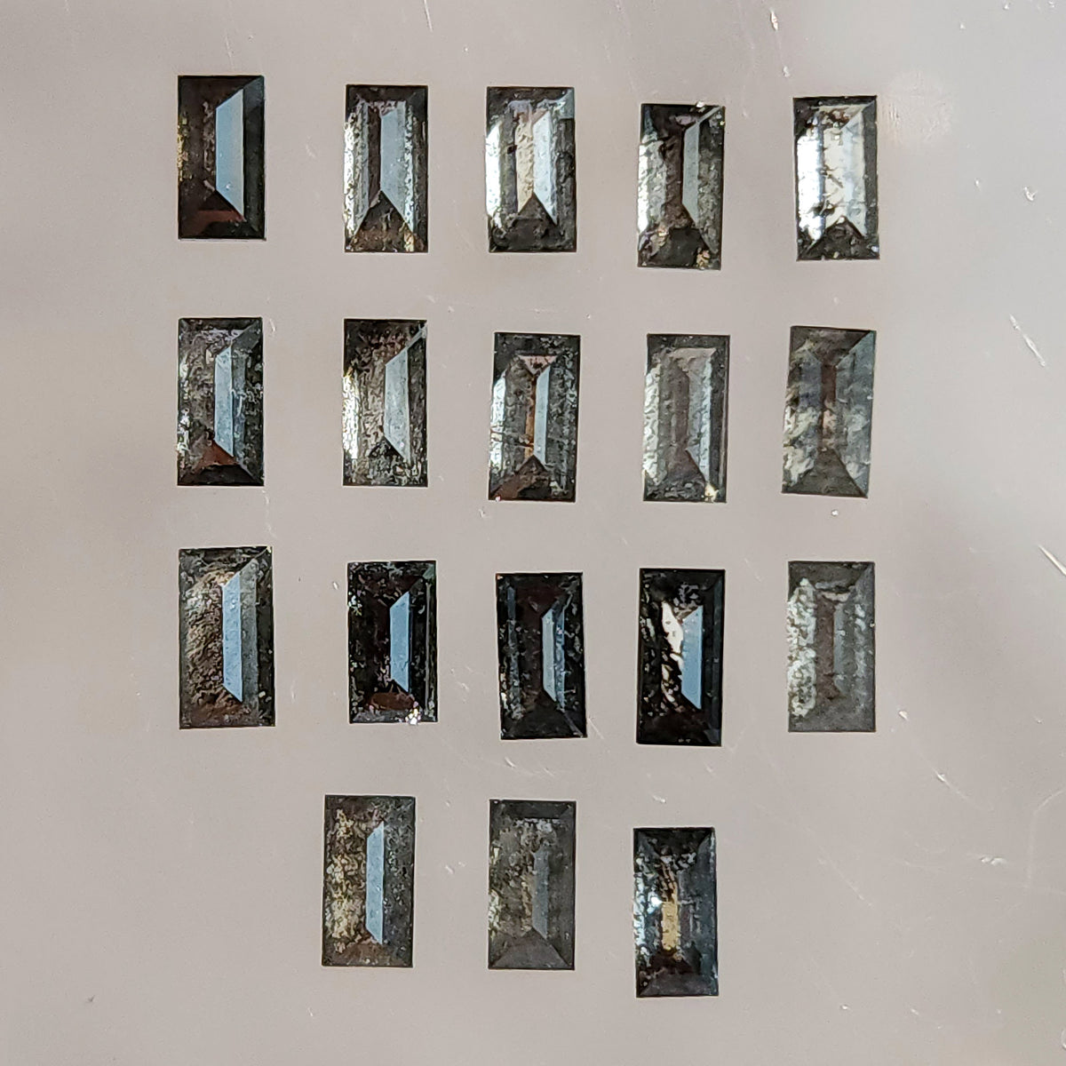 Reverse-side salt and pepper diamond baguettes arranged in rows on a light surface, showing pavilion facets and varied inclusions.